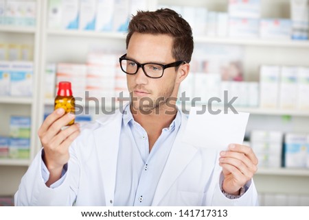 Young male pharmacist checking prescription in front of medicines at drugstore