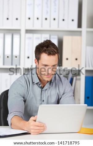 Serious young businessman looking at laptop in office