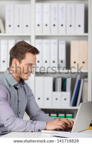 Smiling young businessman using laptop at office desk
