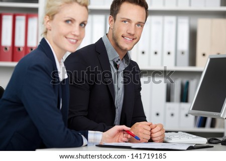 Smiling young businessman and woman in meeting at office desk looking in camera