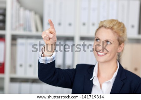 Smiling young female executive pointing upwards in the office