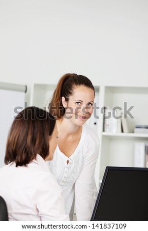 Two young female business colleagues working at a computer together, one looking up and smiling