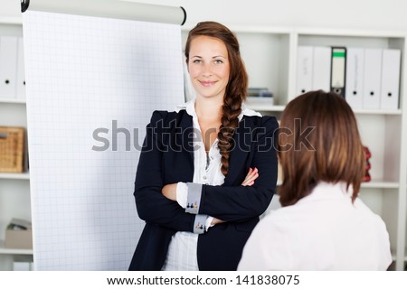 Confident young business woman with a blank white flip chart with copyspace standing smiling at the camera with folded arms