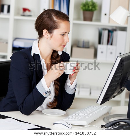 Attractive young female executive having coffee while going through a mail in her computer.