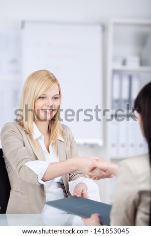 Young businesswoman shaking hands with female candidate at office desk