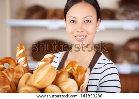 smiling salesgirl working in bakery and holding basket with bread loafs