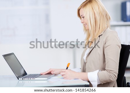 Side view of young businesswoman drawing bar graph while looking at laptop at office desk
