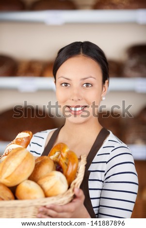 beautiful young woman working in bakery showing basket with bread loafs
