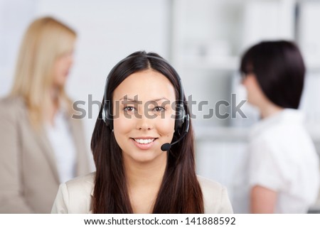 Portrait of Asian female customer service representative wearing headset with female coworkers in background in office