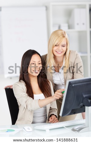 Happy businesswomen pointing at computer while coworker looking at it in office