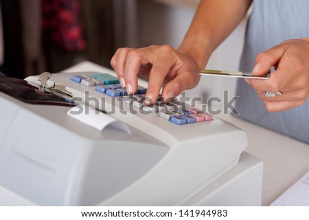 Midsection of saleswoman holding credit card while using cash desk at boutique counter
