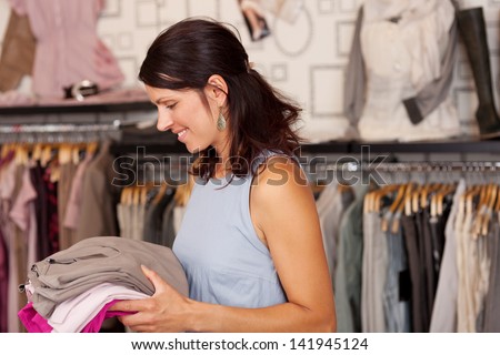 Portrait of happy Saleswoman holding stack of clothes in boutique