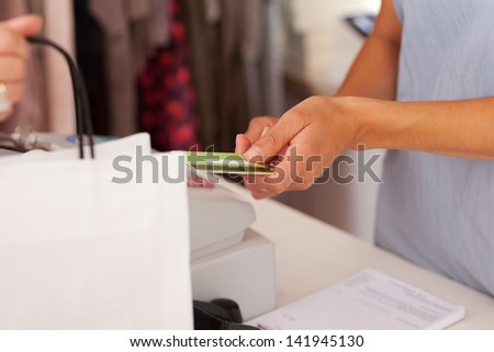 Midsection of saleswoman holding credit card from customer while using cash desk at boutique counter