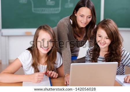 Cheerful teacher teaching her two students with laptop inside the classroom