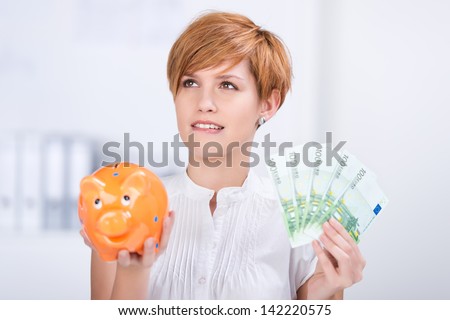 Portrait of businesswoman holding Euro notes and piggy bank in office