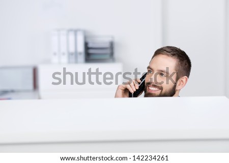 Happy young businessman looking away while on call in office cubicle