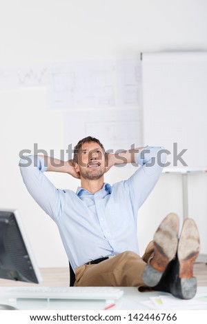 Happy thoughtful businessman with hands behind head looking up at office desk