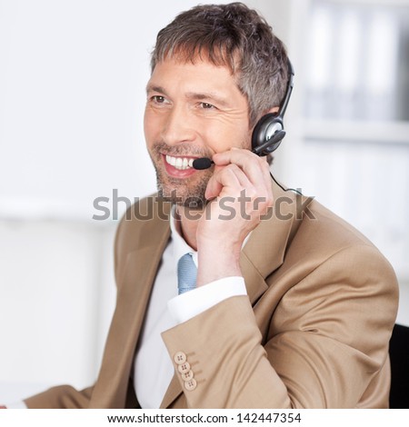 Happy mature male customer service executive conversing on headset at desk in office