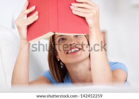 View of an attractive young woman smiling while reading a book viewed from under the book