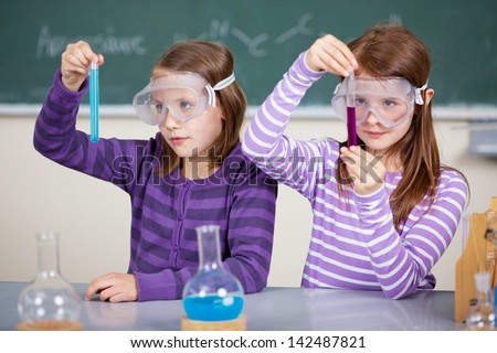 Two female students at the table with chemical reagents and holds test tube in his hands