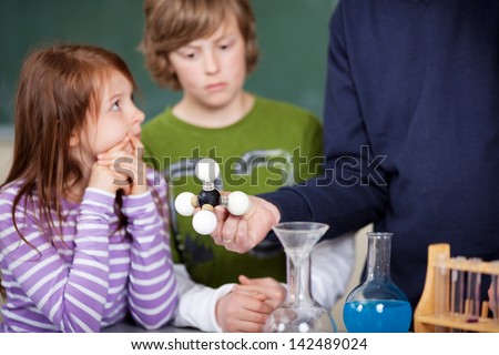 Teacher explaining an atomic model to two attentive young schoolchildren in chemistry class