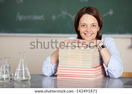 Smiling teacher sitting with book stacks on the table