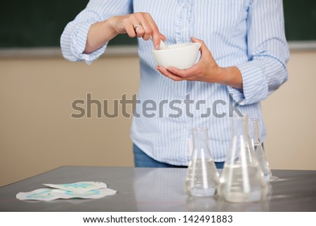 Teacher grinding chemicals in a ceramic pestle in mortar during chemistry class in the classroom