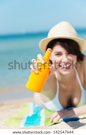 Happy woman shows the sun lotion spray over the blurred beach background