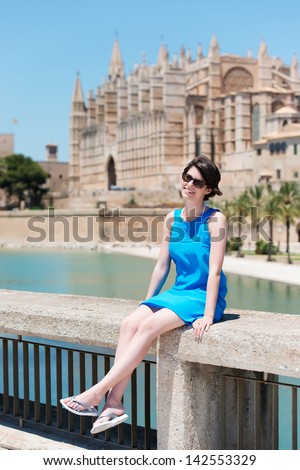 Portrait of lovely young girl sitting on a bridge hand-rail in the park in palma de mallorca
