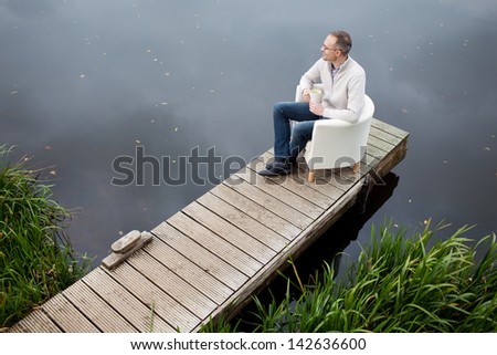 High angle view of mature man holding coffee mug while looking away at pier