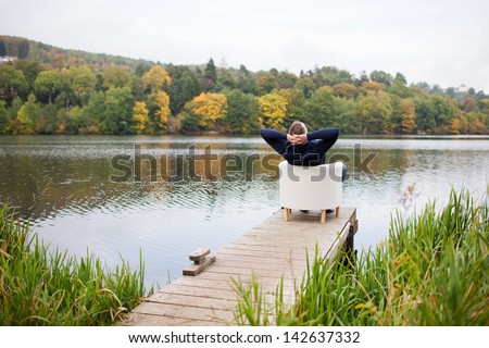 Rear view of mature man with hands behind head relaxing on chair at pier