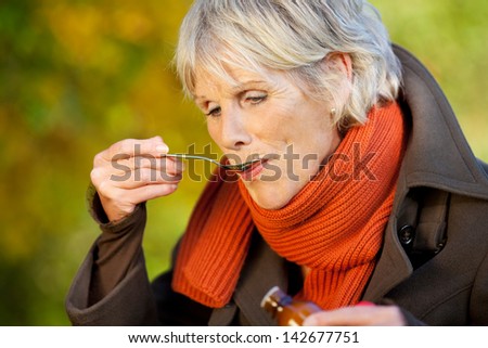 Senior woman in jacket drinking cough syrup at park