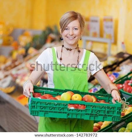 Happy female worker in a supermarket holding a large plastic tray of fresh produce in her hands