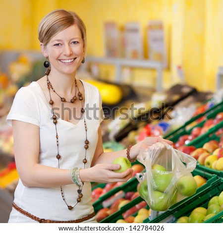 Portrait of young woman filling plastic bag with apples in grocery store