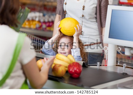 Little girl giving muskmelon to female cashier at counter for billing in supermarket