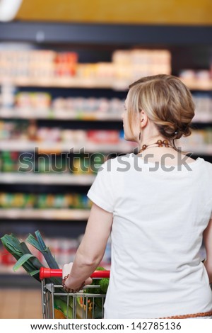 Rear view of young woman with shopping cart at supermarket