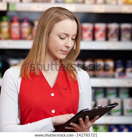Beautiful saleswoman reading checklist on clipboard in grocery store