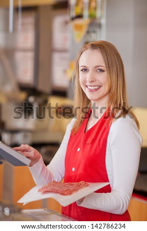 Portrait of happy saleswoman preparing meat bill at counter in grocery store
