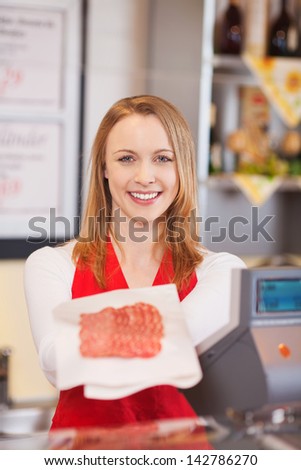 Portrait of confident female worker displaying sliced meat in grocery store