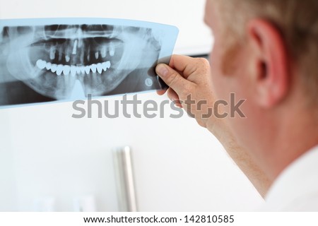 Image of male doctor holding and looking at dental x-ray