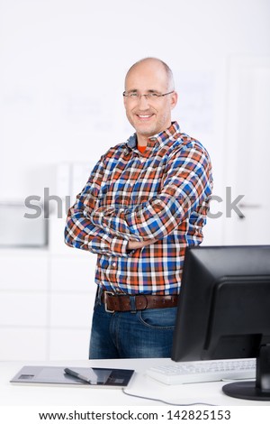 Portrait of confident businessman with arms crossed standing at desk in office