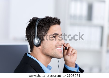 Closeup of young male customer service executive conversing on headset in office
