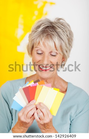 Happy senior woman choosing color from swatches against half painted wall