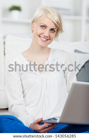 Cute thoughtful young woman sitting on couch with laptop at home