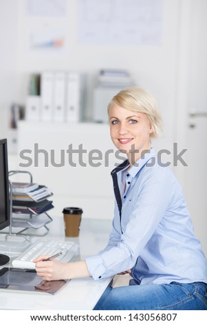 Side view of a young smiling businesswoman sitting at office desk