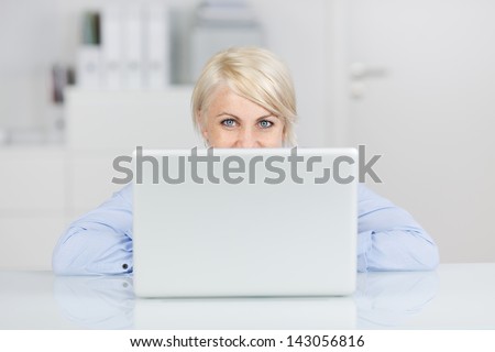 Young smiling blond woman in office looking up in front of a laptop