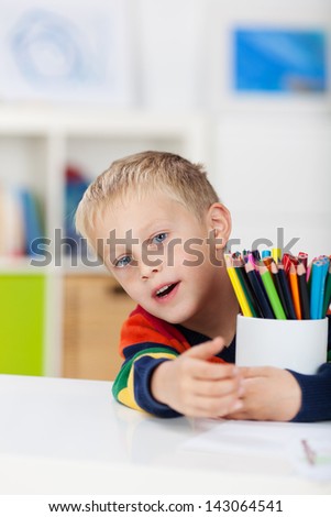 Portrait of little boy with colored pencils at table in house