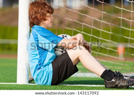 sad looking boy leaning at goal on soccer field