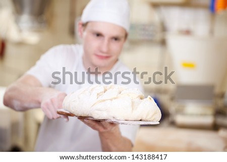Baker putting unbaked bread dough into the hot oven in a bakery with focus to the dough