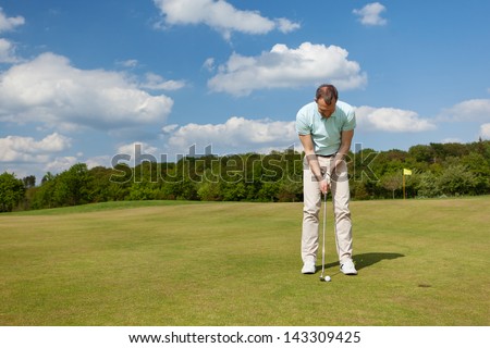 male golfer putting on green against blue sky